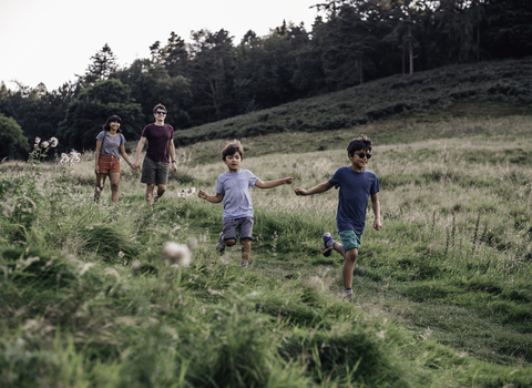 Parents and their two children in a field. The two boys are running down a grass path as their parents walk behind them, smiling