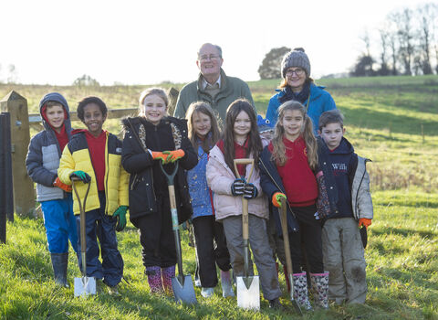 A group of school children with spades, smiling at the camera after planting trees