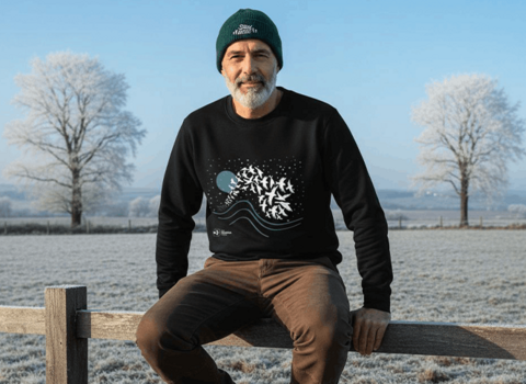 man sat on a fence with a frosty background in a winter jumper