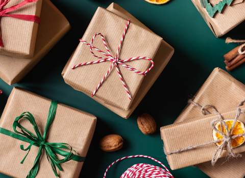A flat lay showing Christmas presents, wrapped in brown paper with colourful string