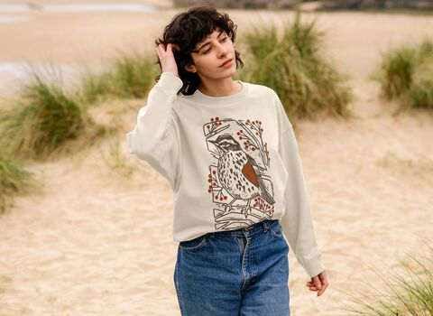A woman on a beach wearing a beige sweatshirt with a redwing graphic design