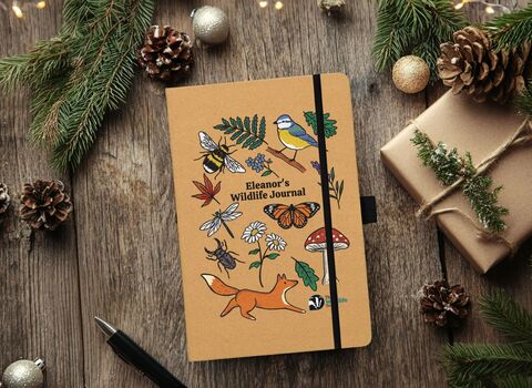 Personalised notebook gift, a brown notebood with illustrations of wildlife, on a christmassy background of pinecones and baubles