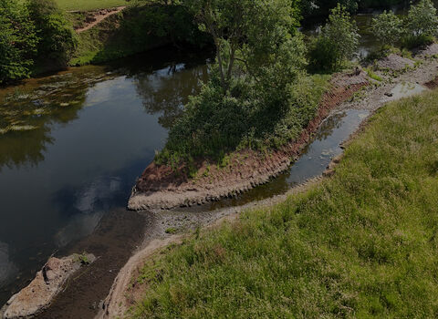 Aerial view of a river with a restored side channel, gravel banks, trees, and surrounding grassland.