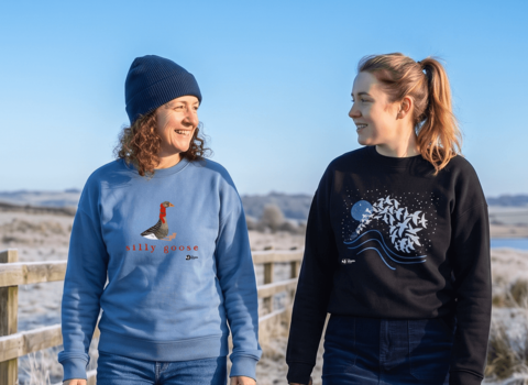 Two women walking in a frosty field wearing the "silly goose" and starling murmuration jumper