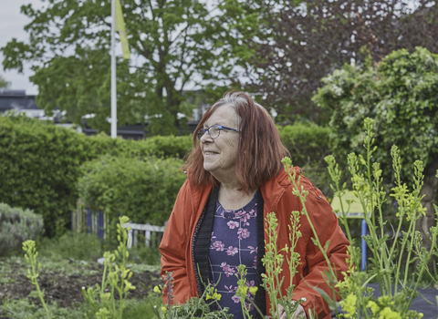 Woman in red coat surrounded by flowers, smiling